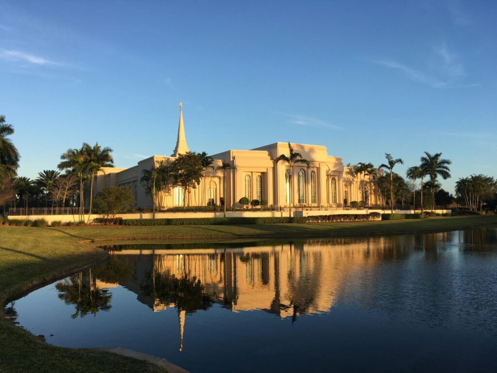 Capture of Fort Lauderdale's LDS Temple reflecting in a pond with palm trees at sunset.