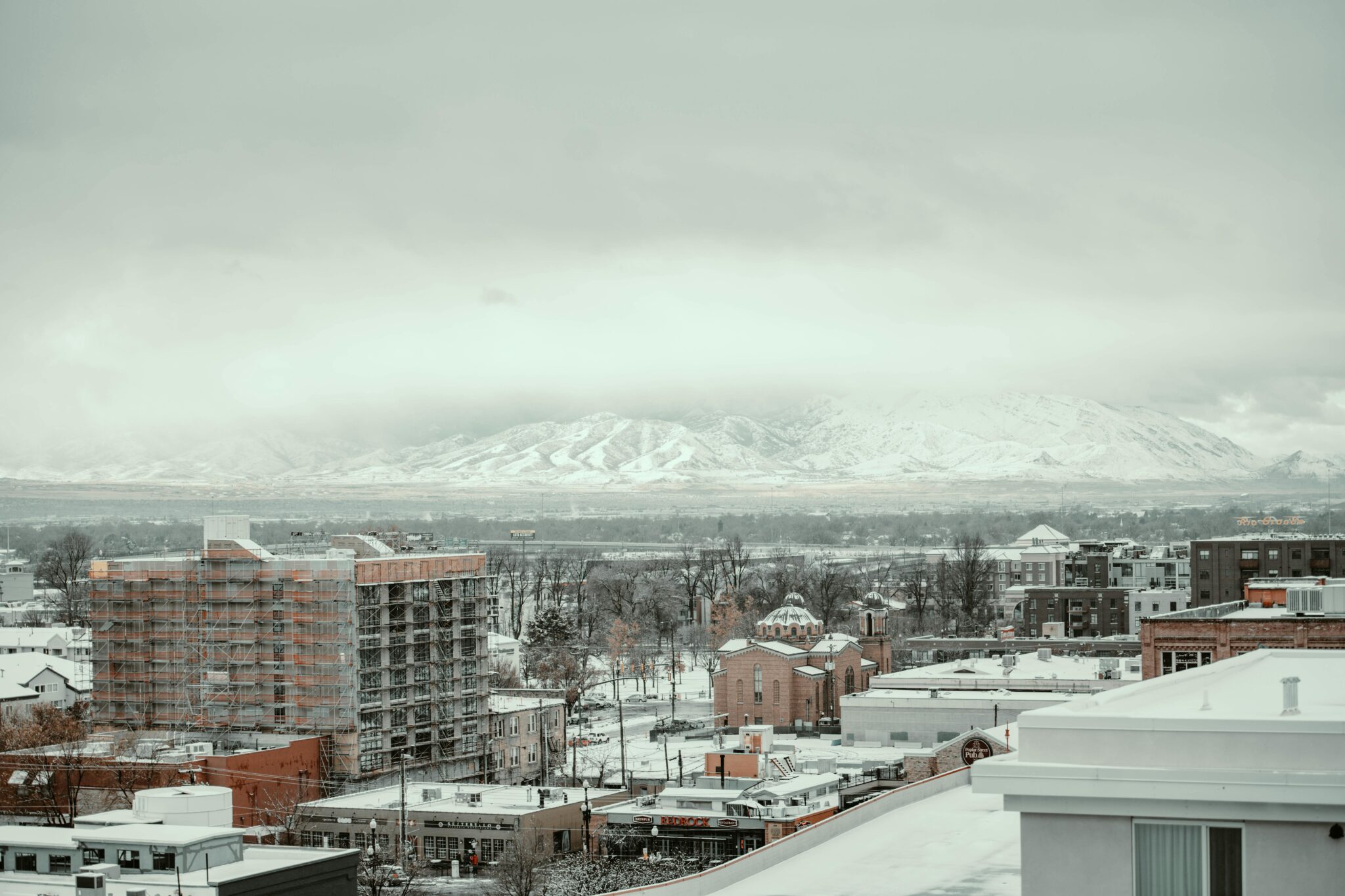 A winter cityscape view in Salt Lake City with snow-covered buildings and mountains in the background.