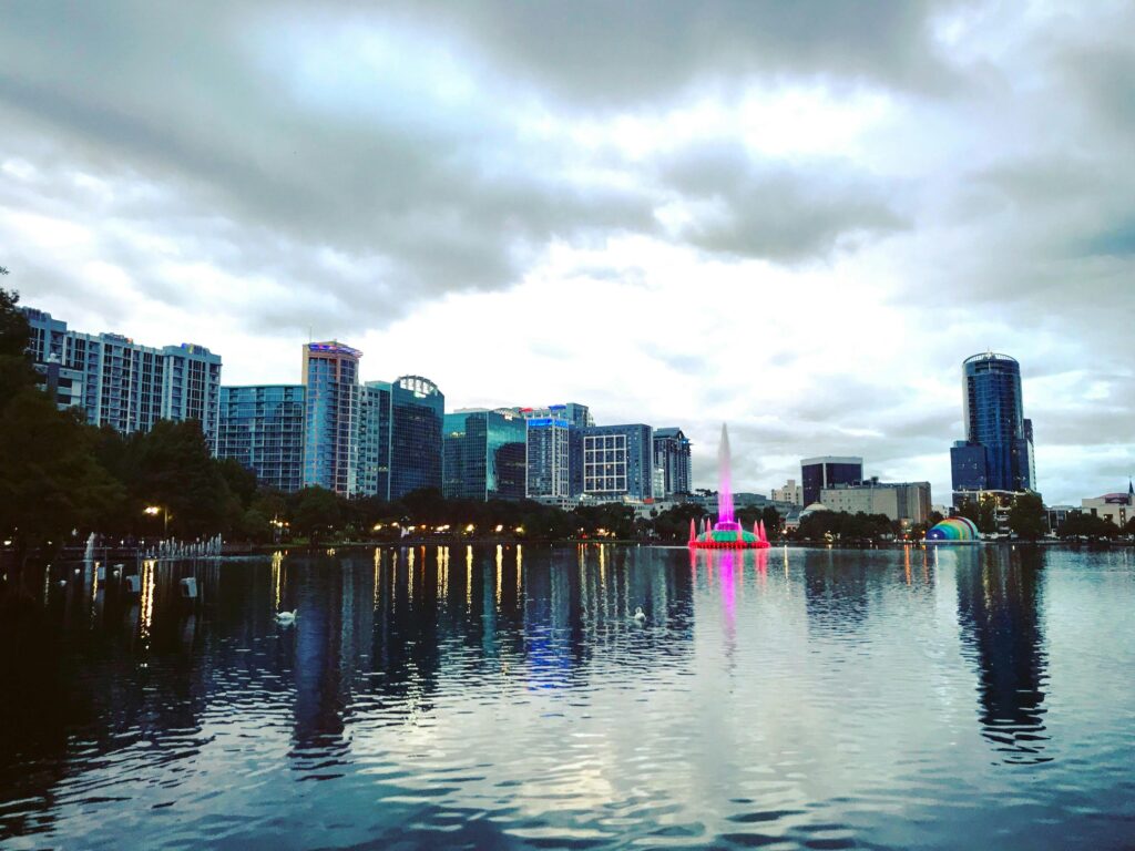Vibrant view of Orlando's skyline reflecting in a lake under a cloudy sky.