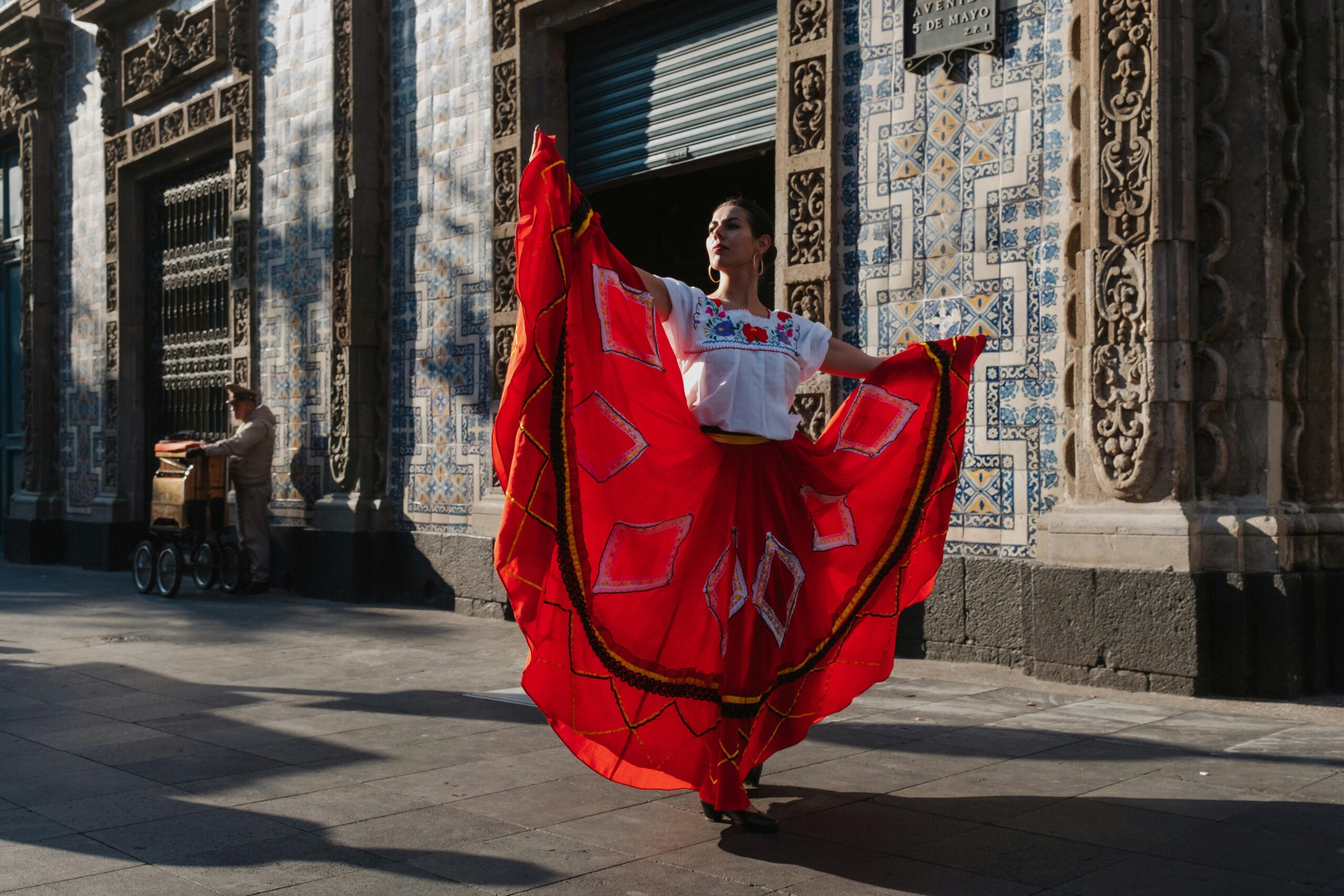 A woman dances gracefully in a vibrant red dress in front of ornate Mexican architecture.
