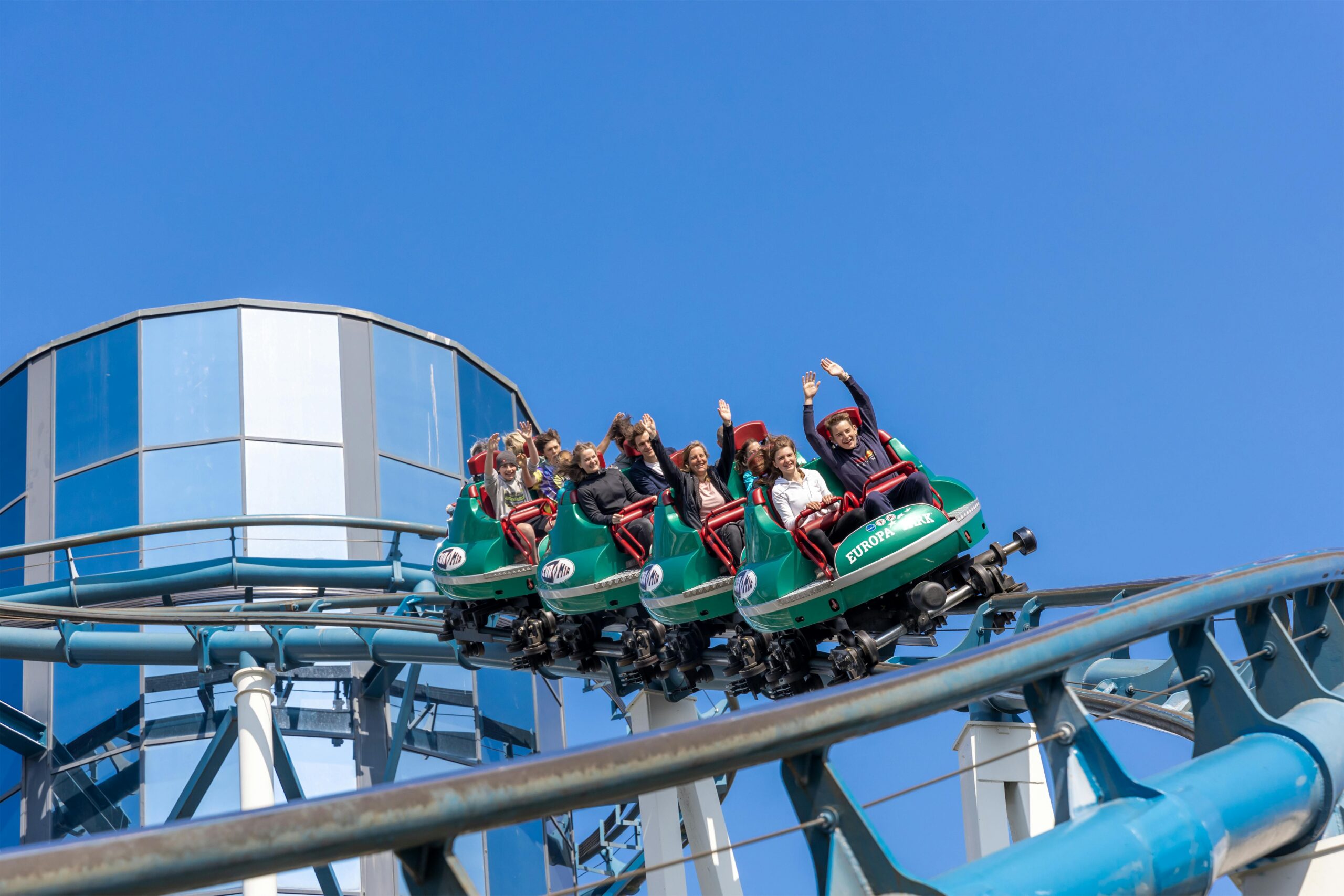 People enjoying a thrilling rollercoaster ride at Europa-Park under a clear blue sky.