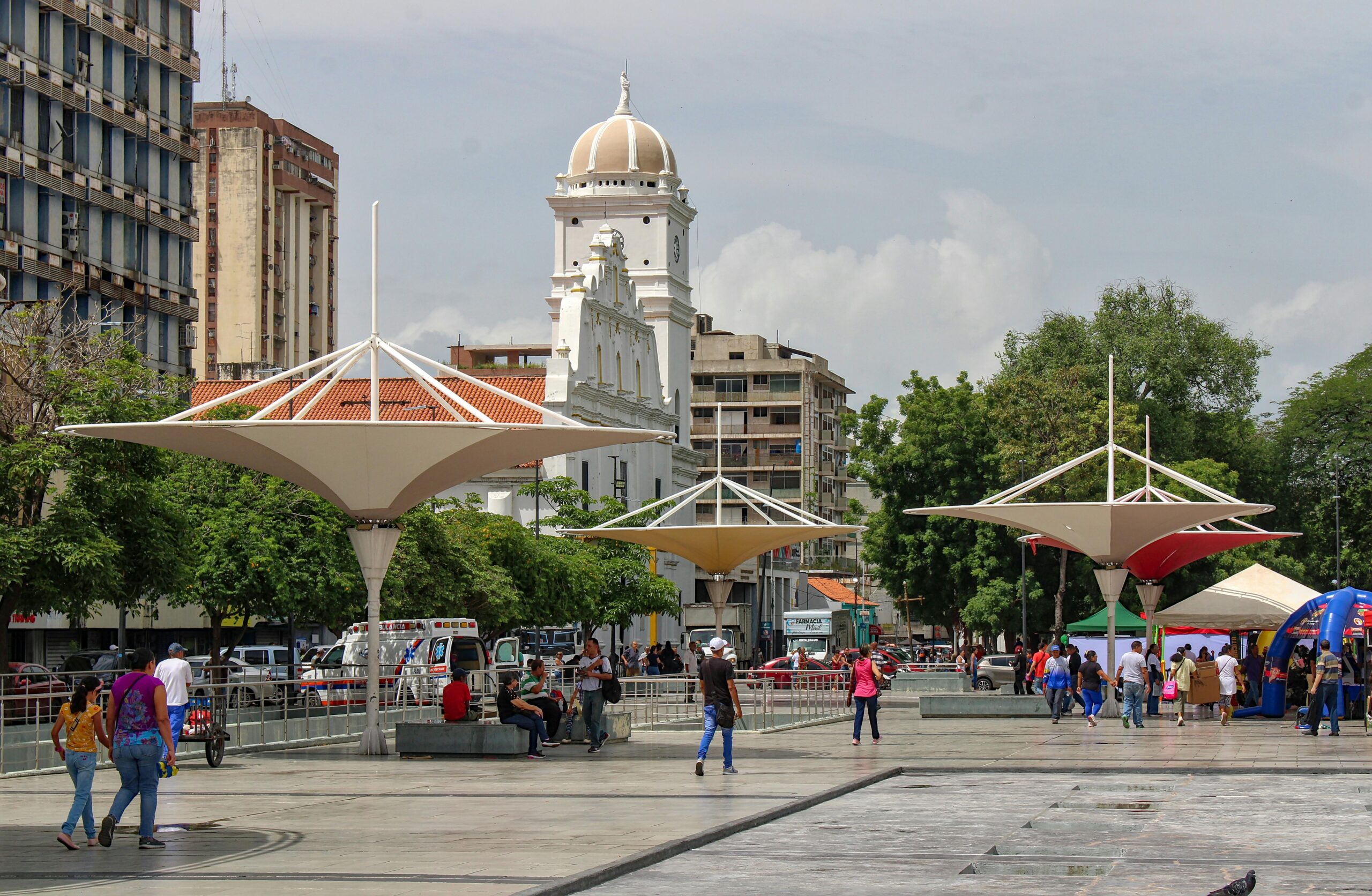 A vibrant city square featuring unique canopies and historic architecture, bustling with people.