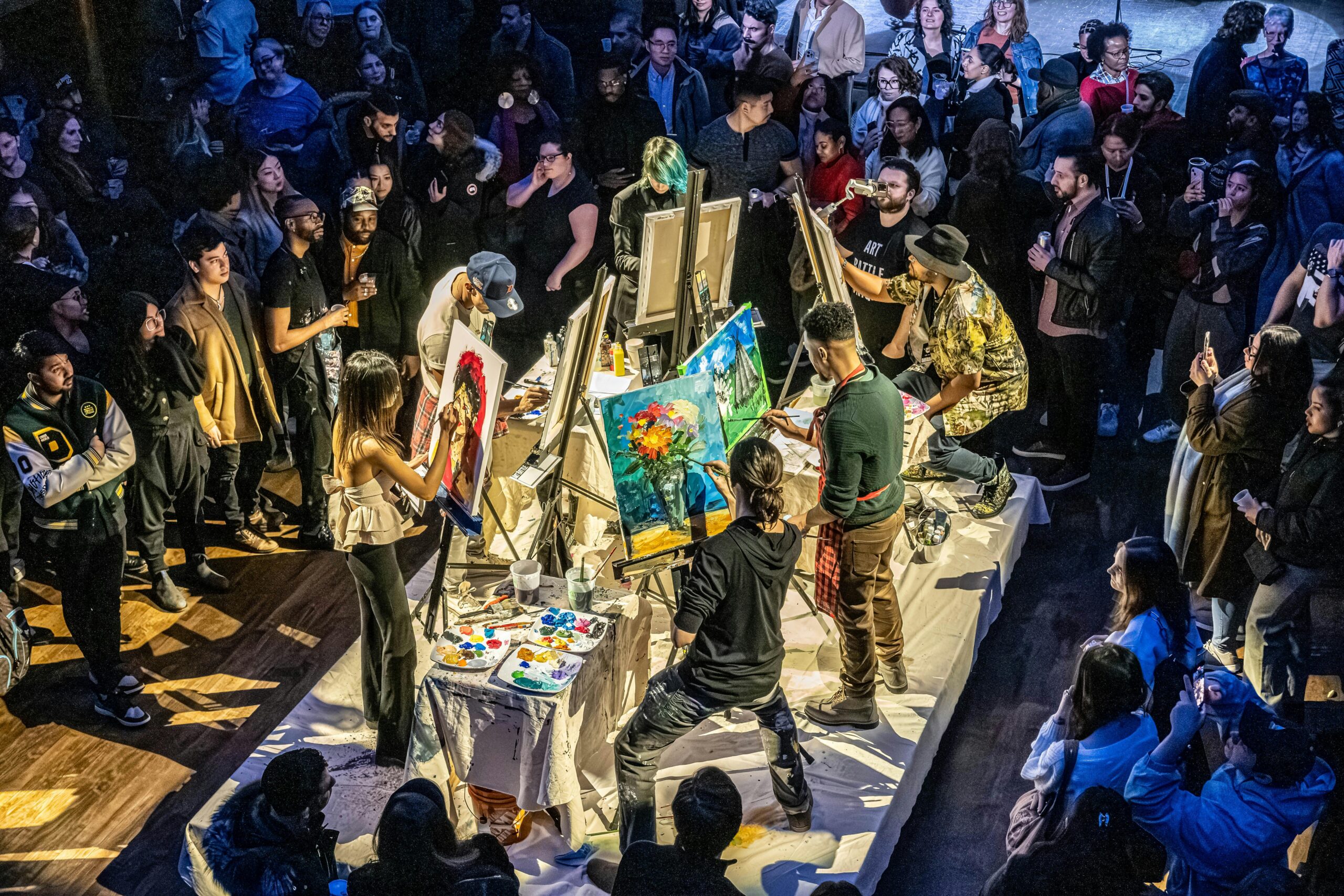 A lively art battle event in Toronto with artists painting in front of an enthusiastic crowd.