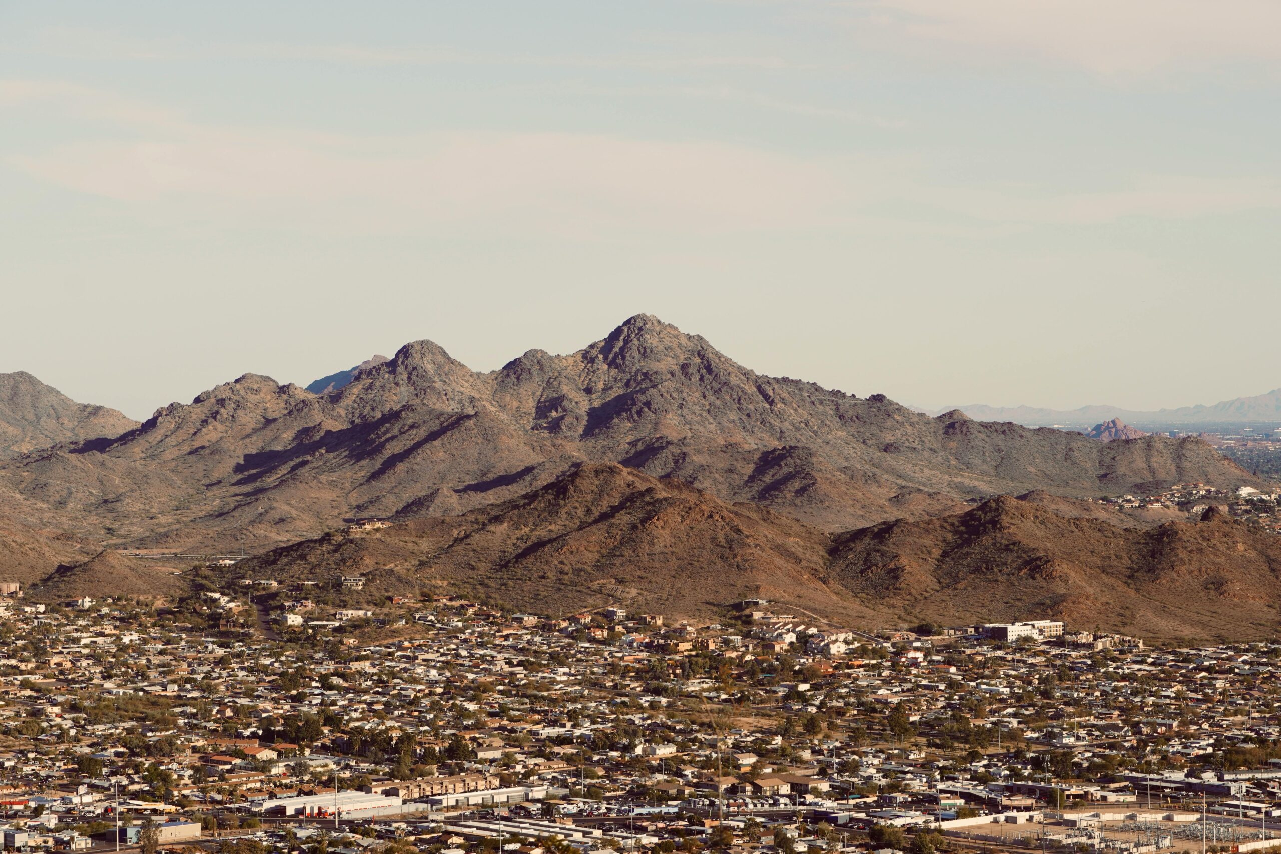 Aerial view of a sprawling city against a rugged mountain backdrop under a clear sky.
