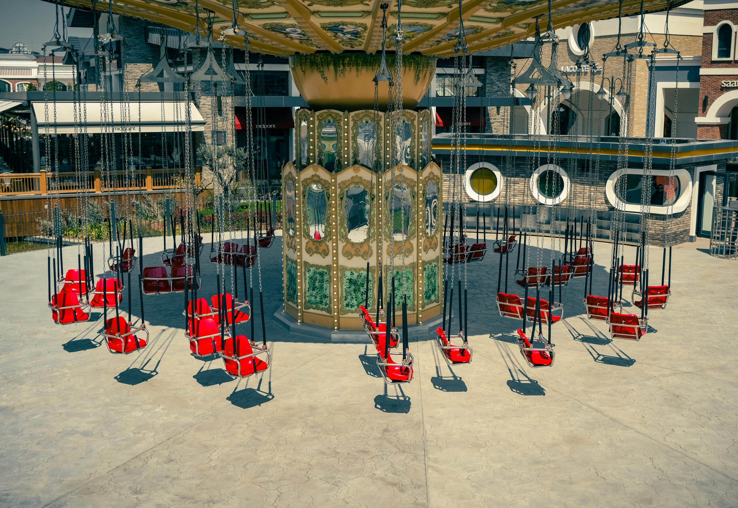An empty carousel with red swing chairs in an İstanbul amusement park on a sunny day.
