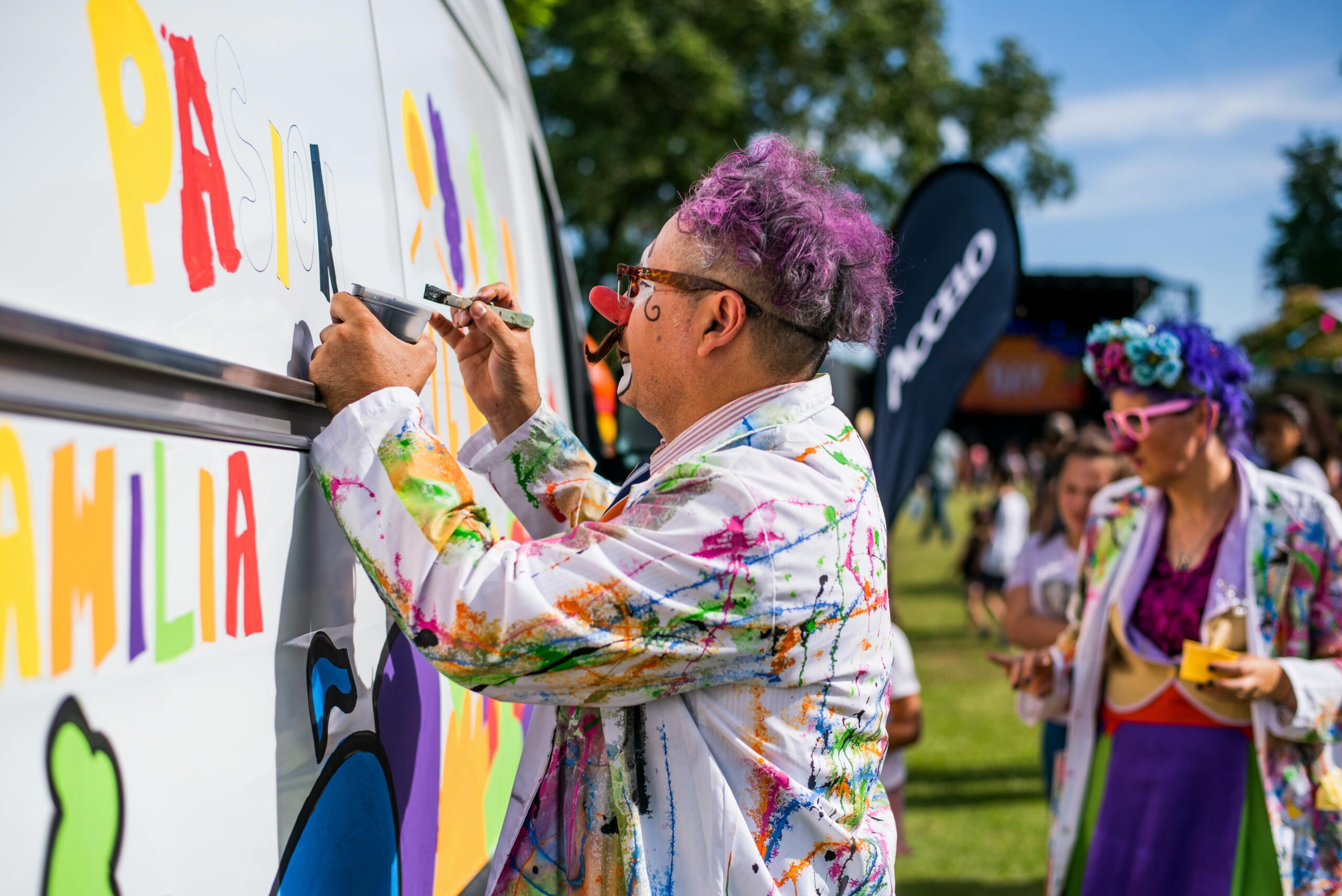 Street artist with colorful hair paints a vibrant mural at an outdoor festival.