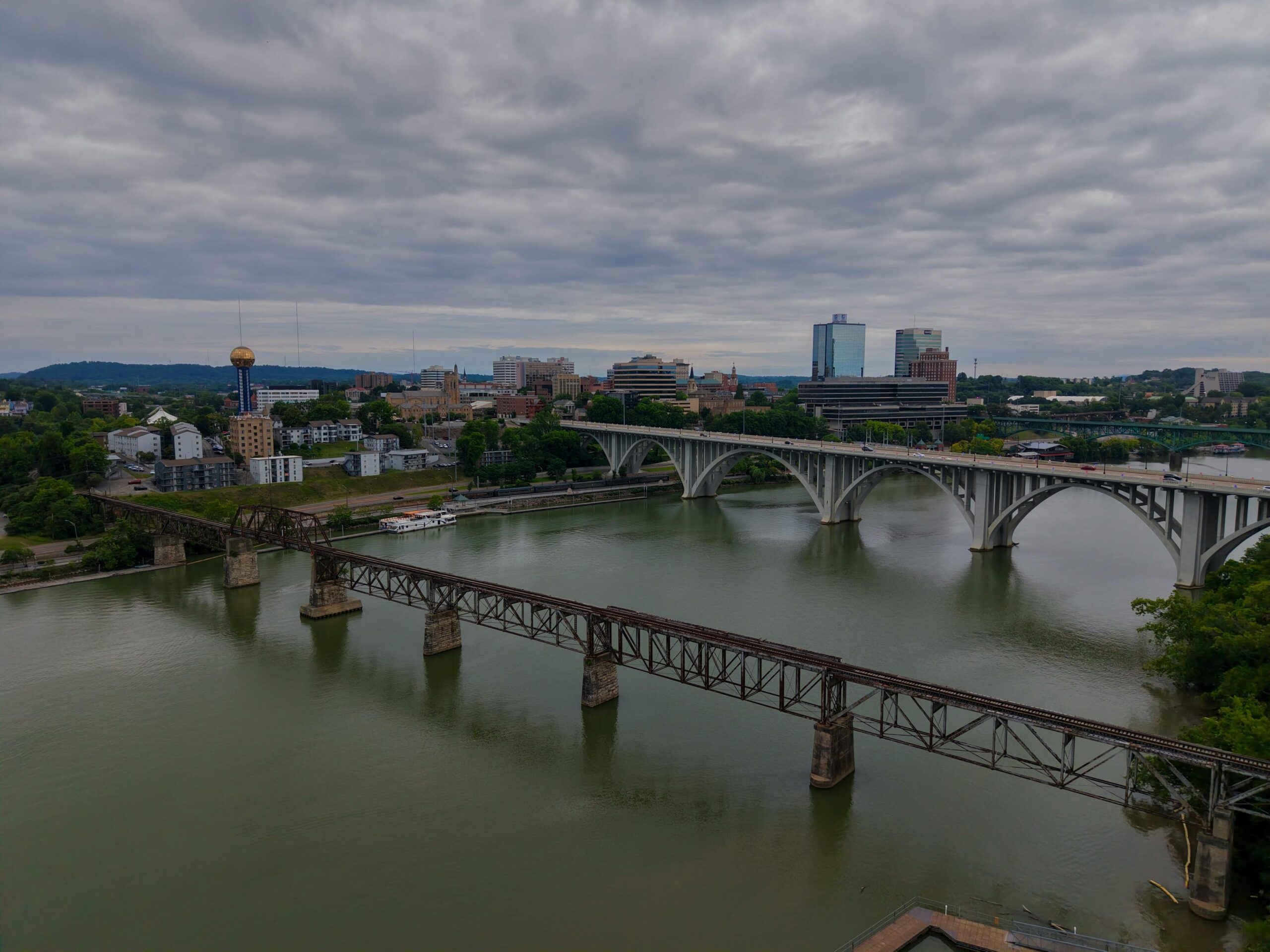 Scenic aerial view of Knoxville's skyline, bridges, and river under cloudy skies.