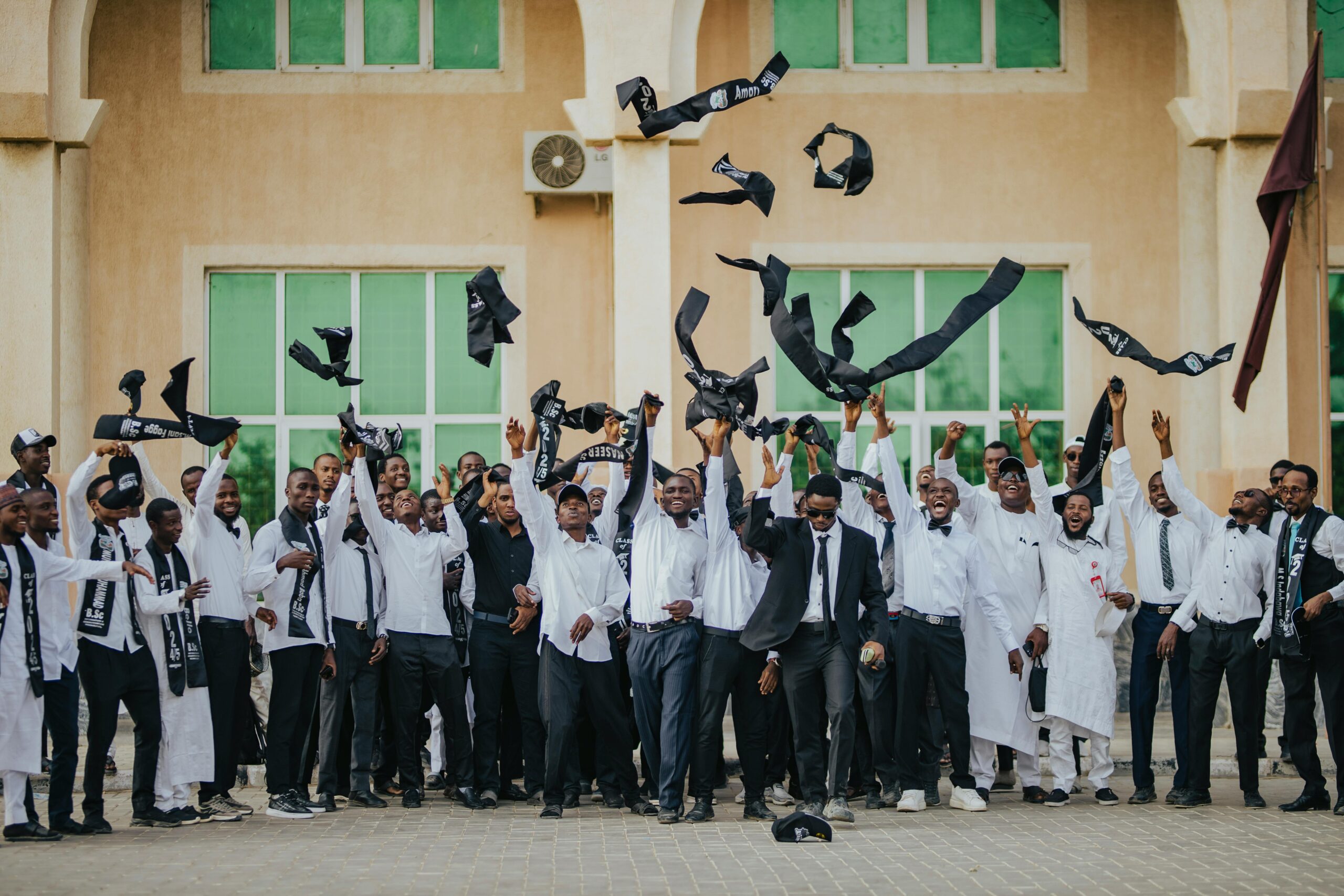 Group of graduating students celebrating with scarves thrown into the air outdoors.