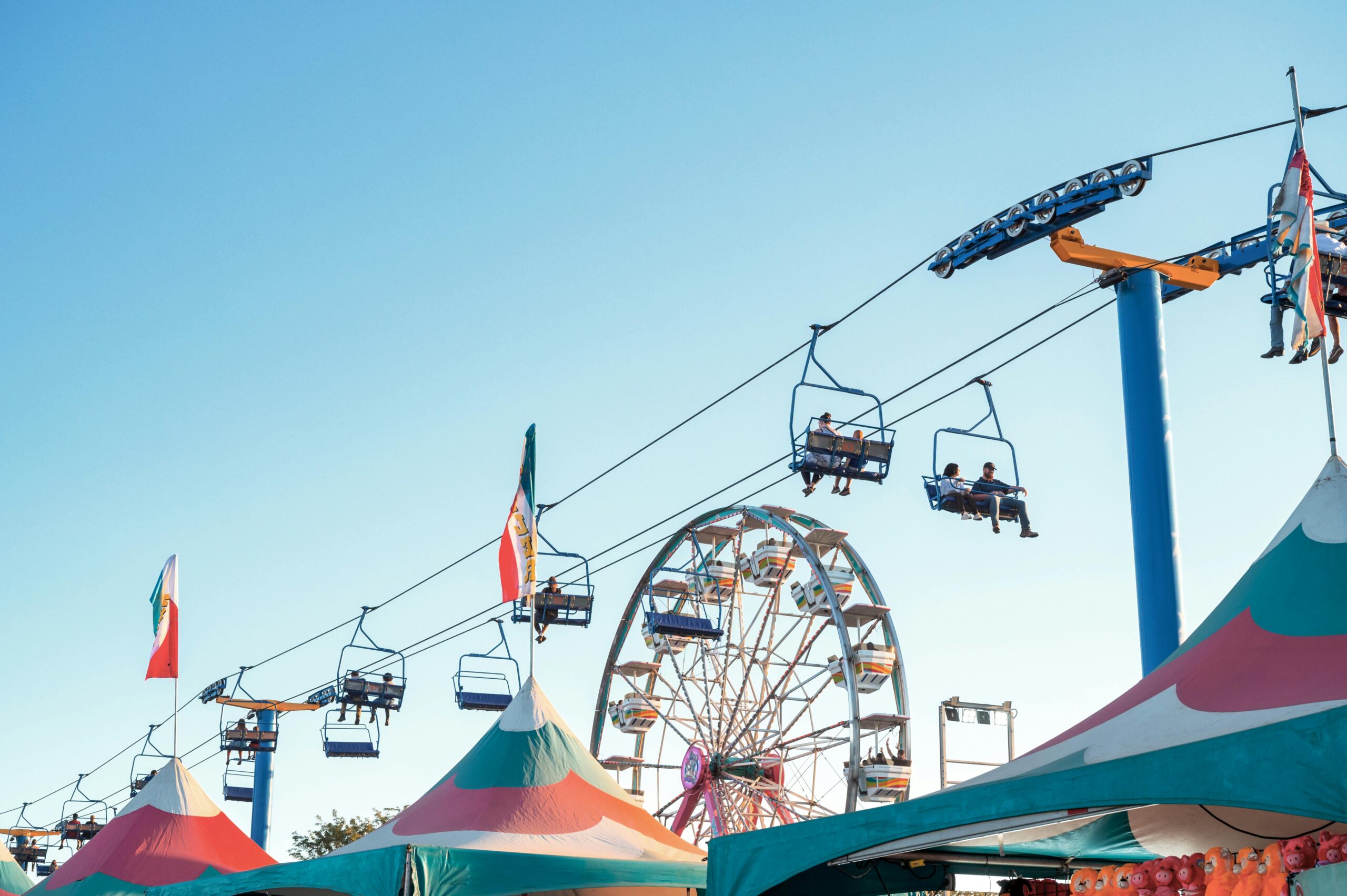 A vibrant carnival scene in Boise, ID, showcasing a Ferris wheel and cable ride under a clear blue sky.