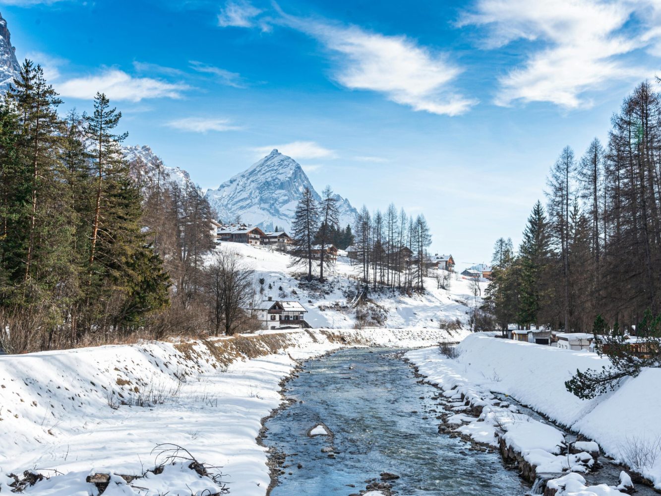 Serene winter scene of a snowy landscape and stream in Cortina d'Ampezzo, Italy.