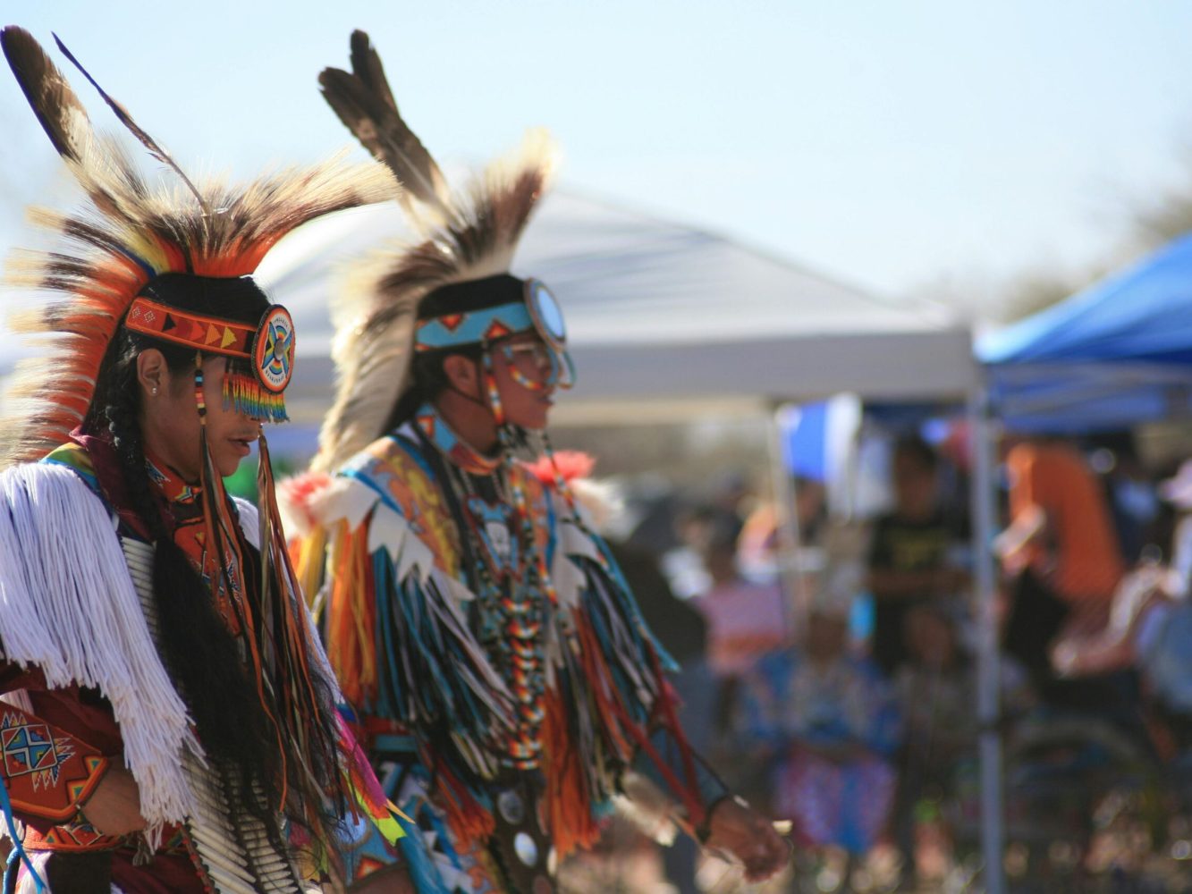 Two Native American dancers in vibrant regalia performing a traditional dance outdoors.
