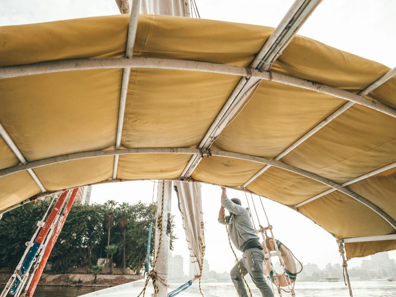 Side view of anonymous male in casual clothes setting sail on traditional boat floating on river on sunny day