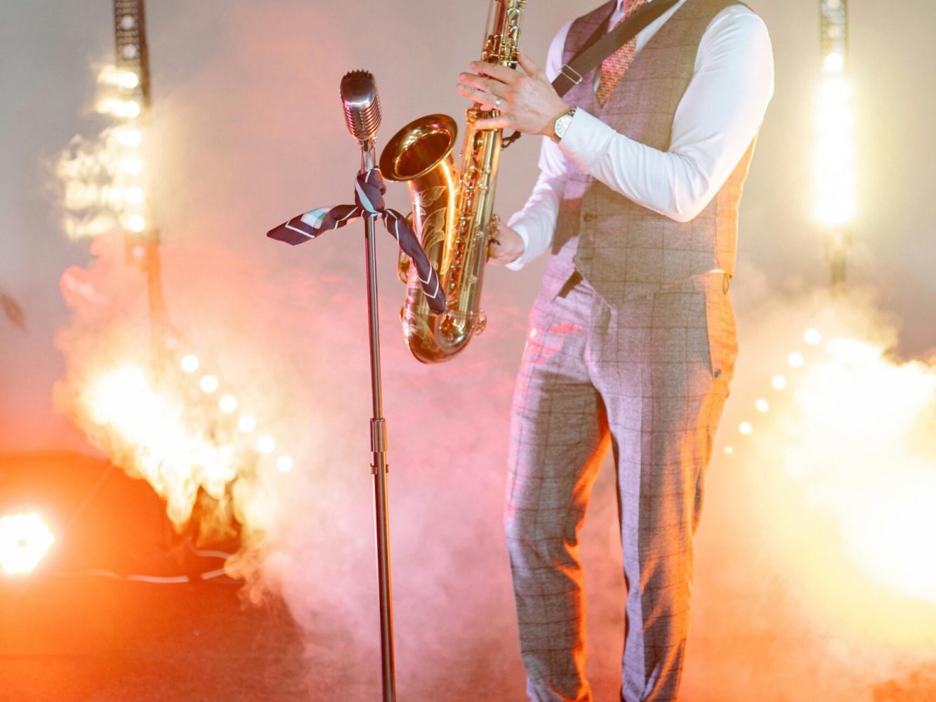 Male saxophonist performing live on a smoke-filled stage with vibrant lighting.